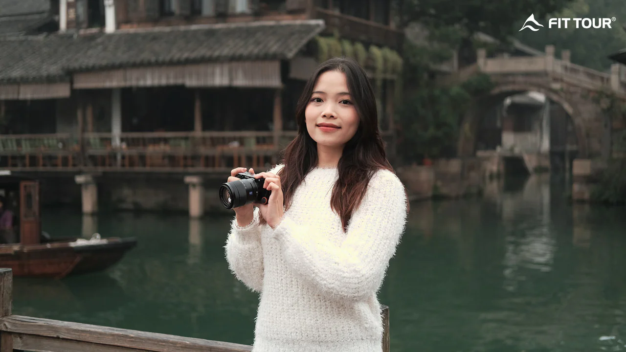 Cô gái cầm máy ảnh tạo dáng bên dòng kênh tại Ô Trấn, Giang Nam, với khung cảnh thơ mộng phía sau