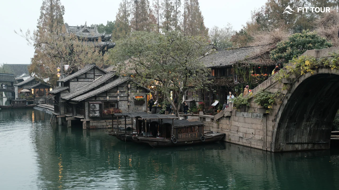 Khung cảnh cổ trang bên dòng nước với cầu đá và thuyền gỗ tại ngôi làng cổ