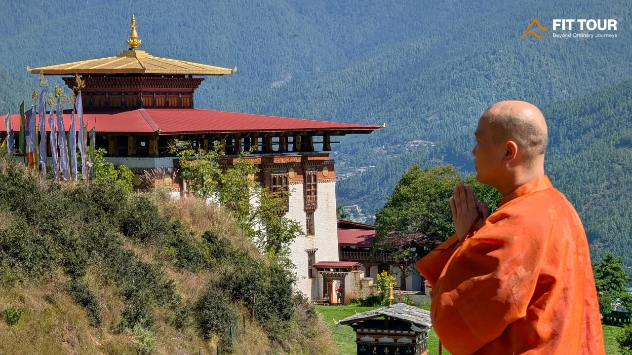 Tăng sĩ đứng trước Wangditse Lhakhang với thung lũng Thimphu và núi rừng phía sau